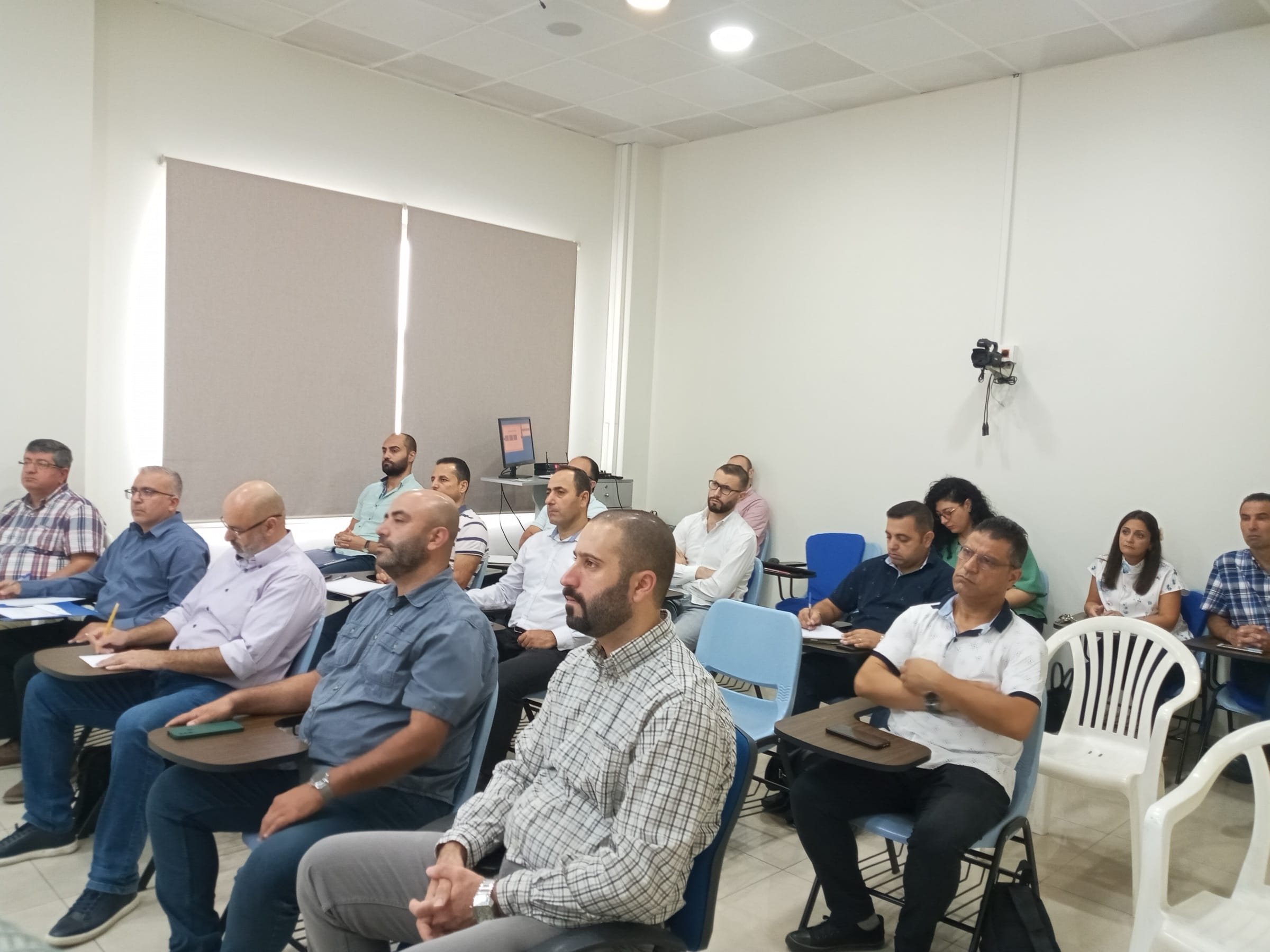 A full cohort of CAIT students seated in a bright classroom during an orientation session, papers in hand, facing the front of the room.